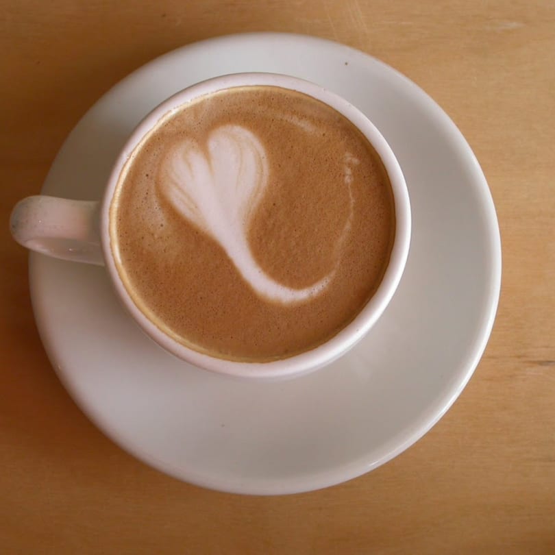 Overhead view of a latte with a heart design in the foam, on a white saucer.