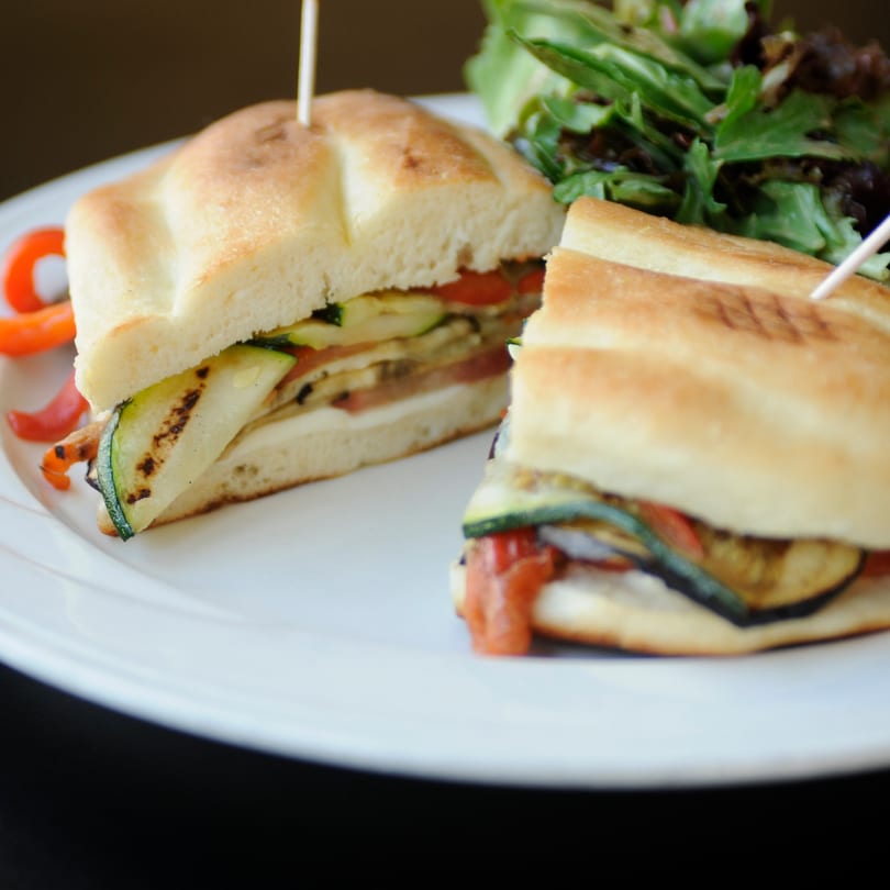 Grilled vegetable panini with zucchini, eggplant, tomato, and cheese, served with a side salad.