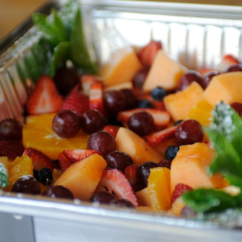 A vibrant fruit salad with strawberries, grapes, melon, and oranges in a silver serving dish.