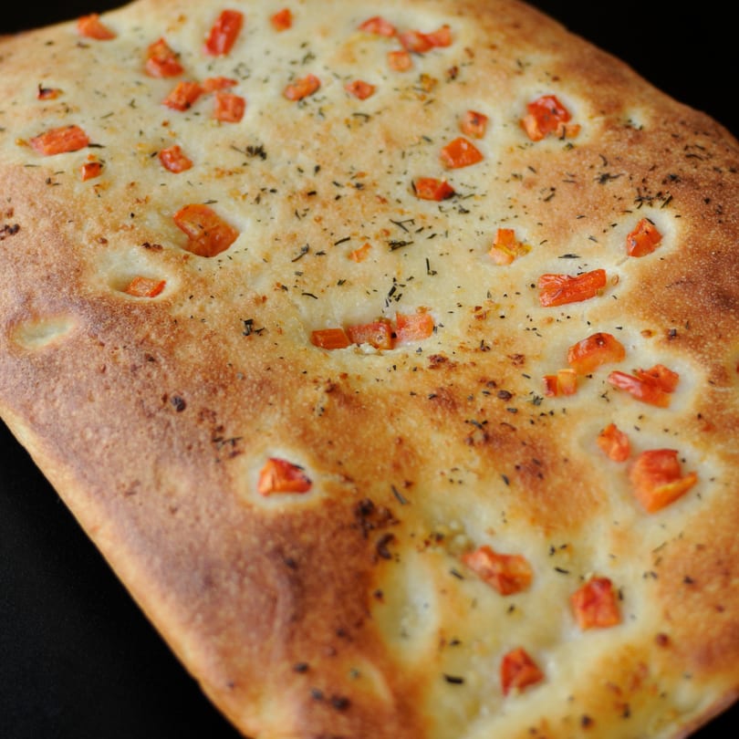 Close-up of golden-brown focaccia bread topped with diced tomatoes and herbs.