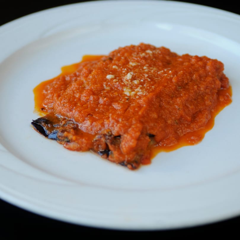 Vivoli Cafe's eggplant parmesan, topped with rich red sauce and grated cheese, on a white plate.