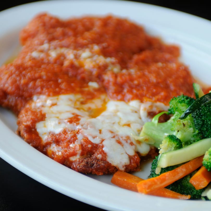 Chicken parmesan with melted cheese and red sauce, served with steamed broccoli and carrots.