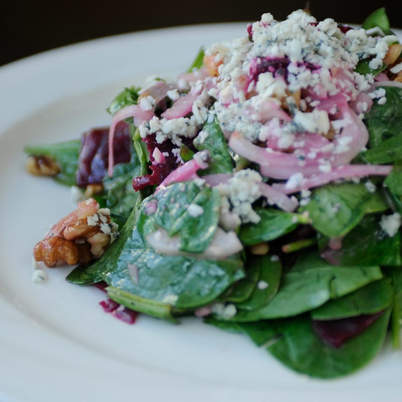 Spinach salad with red onions, walnuts, and crumbled blue cheese on a white plate.