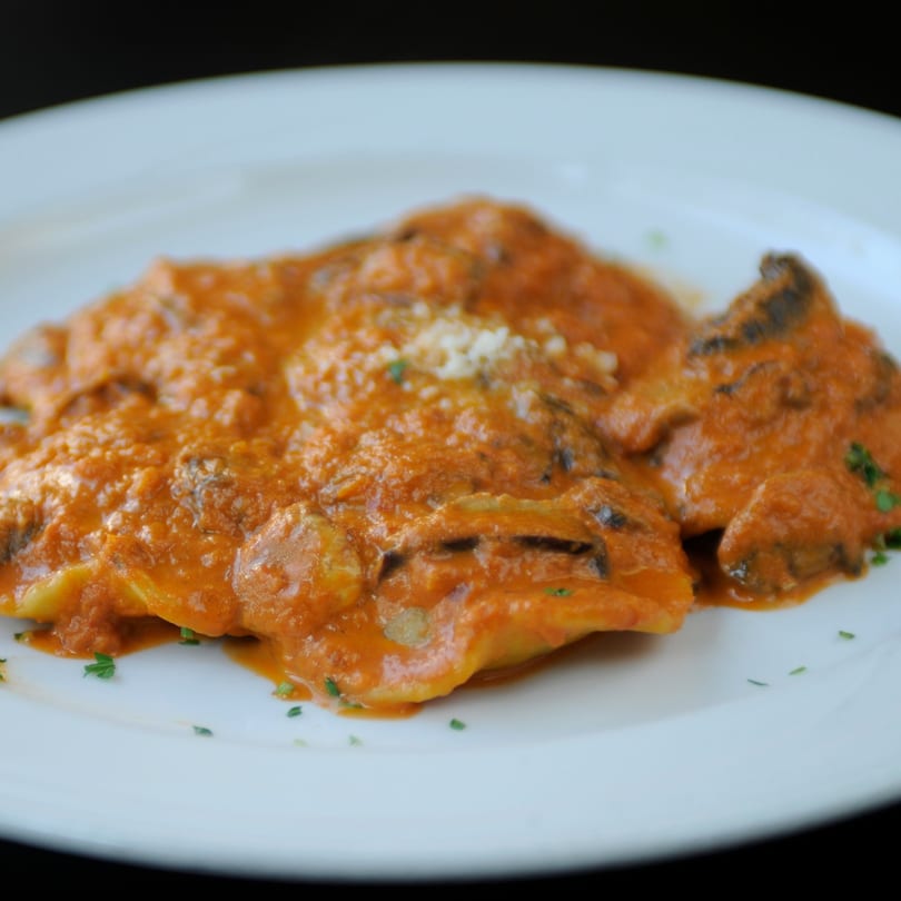 Ravioli with a creamy orange sauce, garnished with parsley and grated cheese on a white plate.